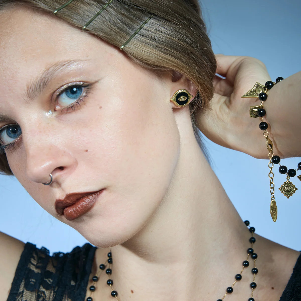 Close portrait showing a gold-tone Mirror Witness Stud Earring with the hair lifted to reveal the black obsidian center.