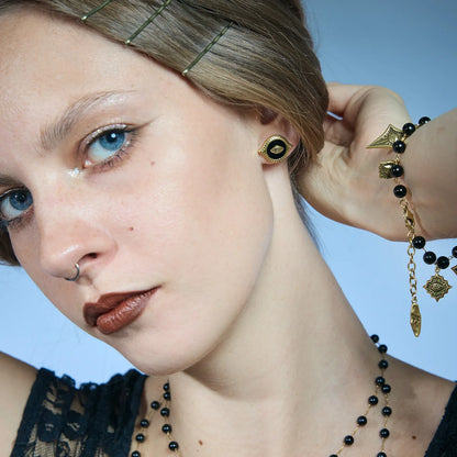 Close portrait showing a gold-tone Mirror Witness Stud Earring with the hair lifted to reveal the black obsidian center.