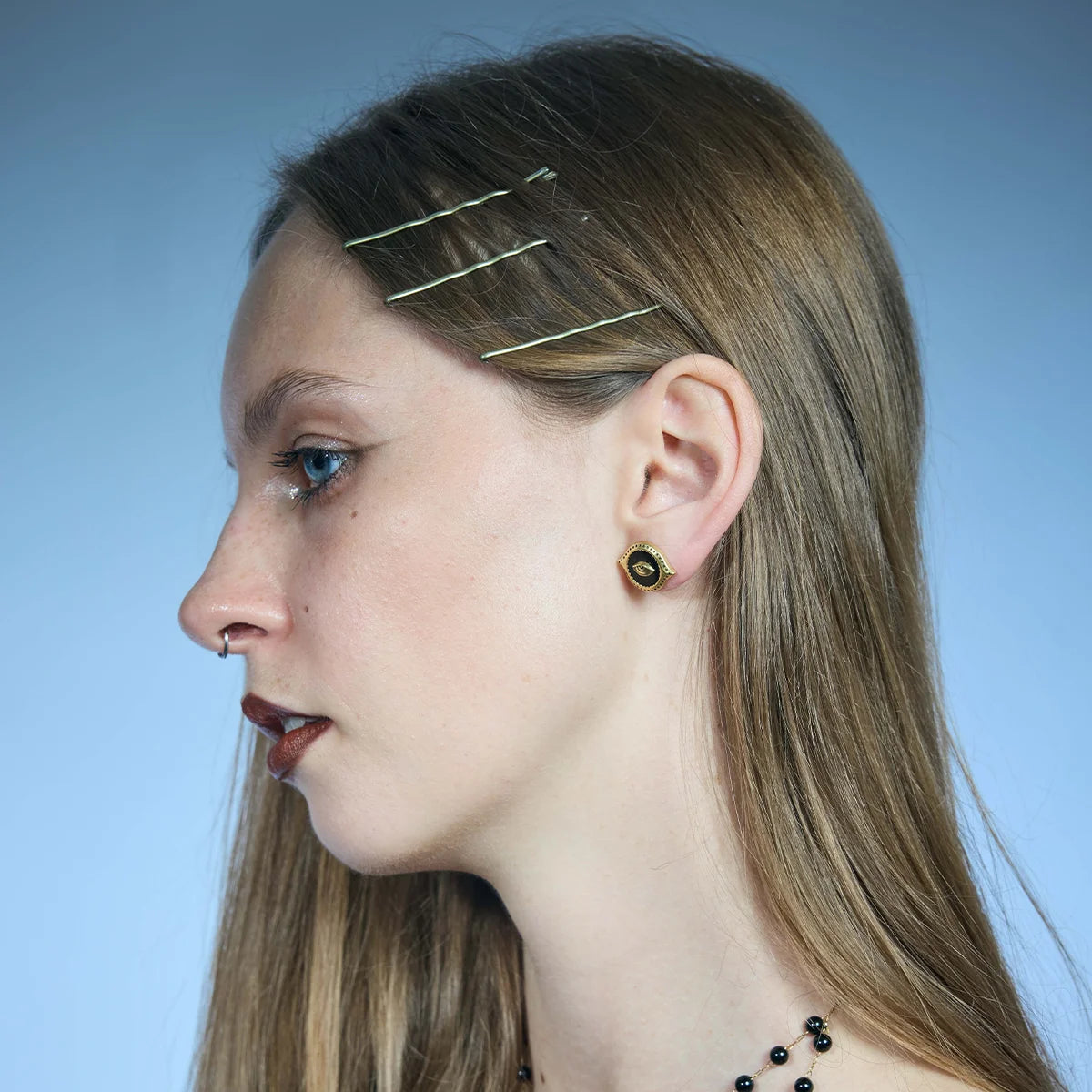 Side portrait showing a gold-tone Mirror Witness Stud Earring sitting close to the lobe with a raised eye motif.