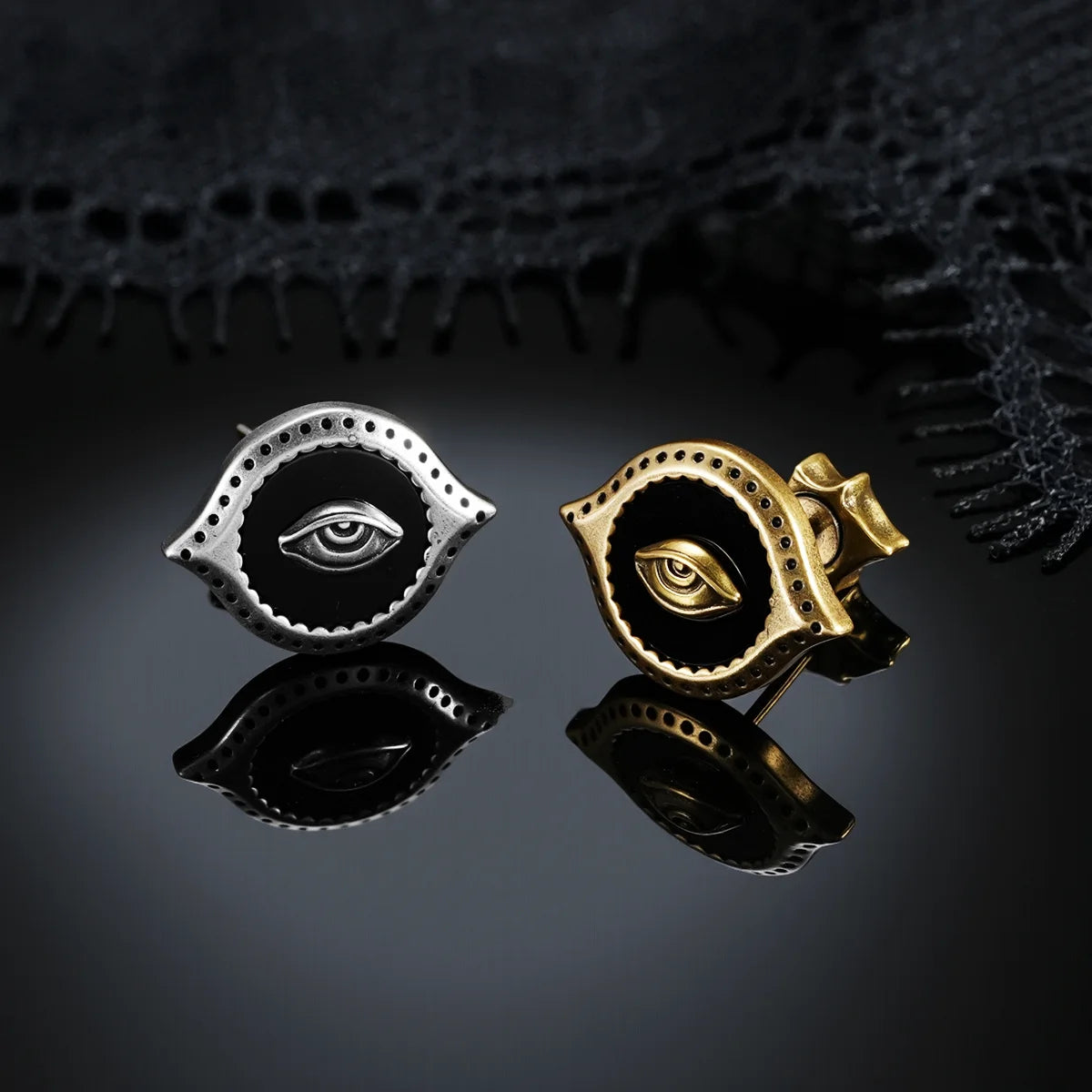 Antiqued silver- and gold-tone Mirror Witness Stud Earrings displayed together on a dark reflective surface beneath black lace.