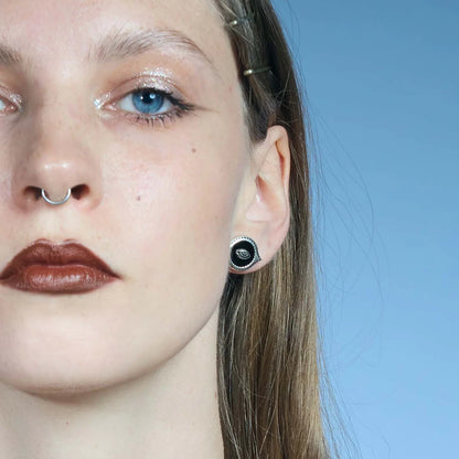 Front close-up of an antiqued silver-tone Mirror Witness Stud Earring with a raised eye motif over a black obsidian center.