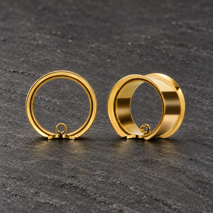 Pair of gold-tone Modular Ring tunnels on natural gray slate, showing front and angled views with small attachment loops.