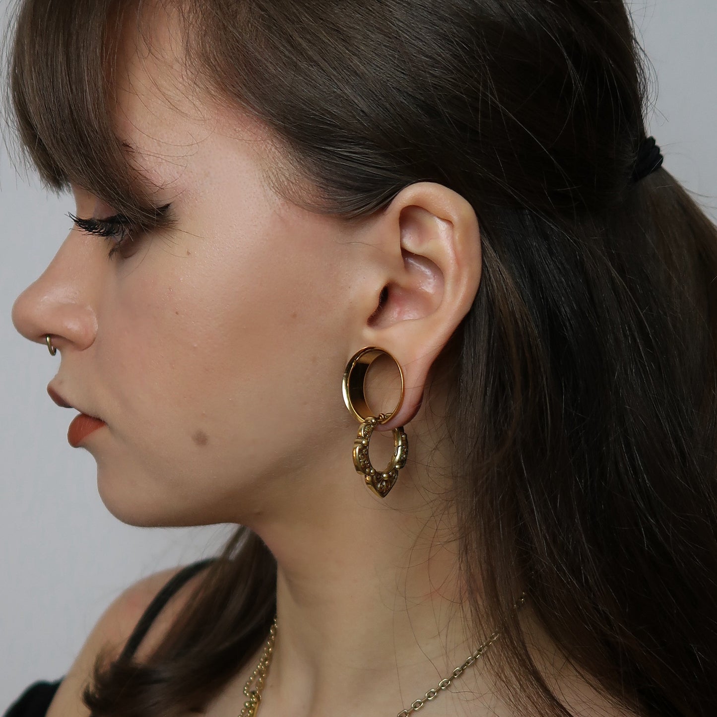 Gold-tone modular ring tunnel worn in earlobe with an ornate teardrop charm hanging below