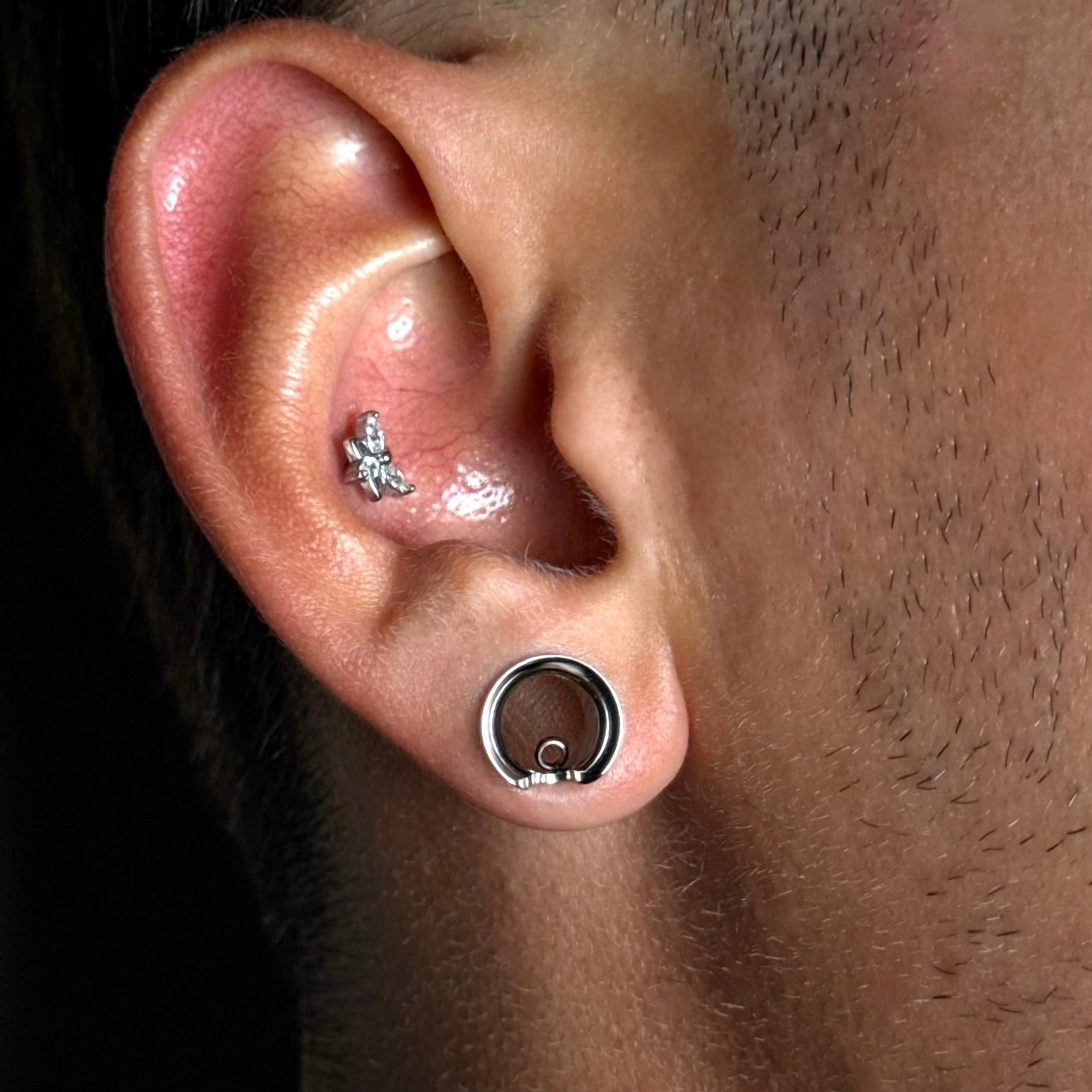 Silver-tone modular ring tunnel worn in earlobe with a small stud in the upper ear cartilage