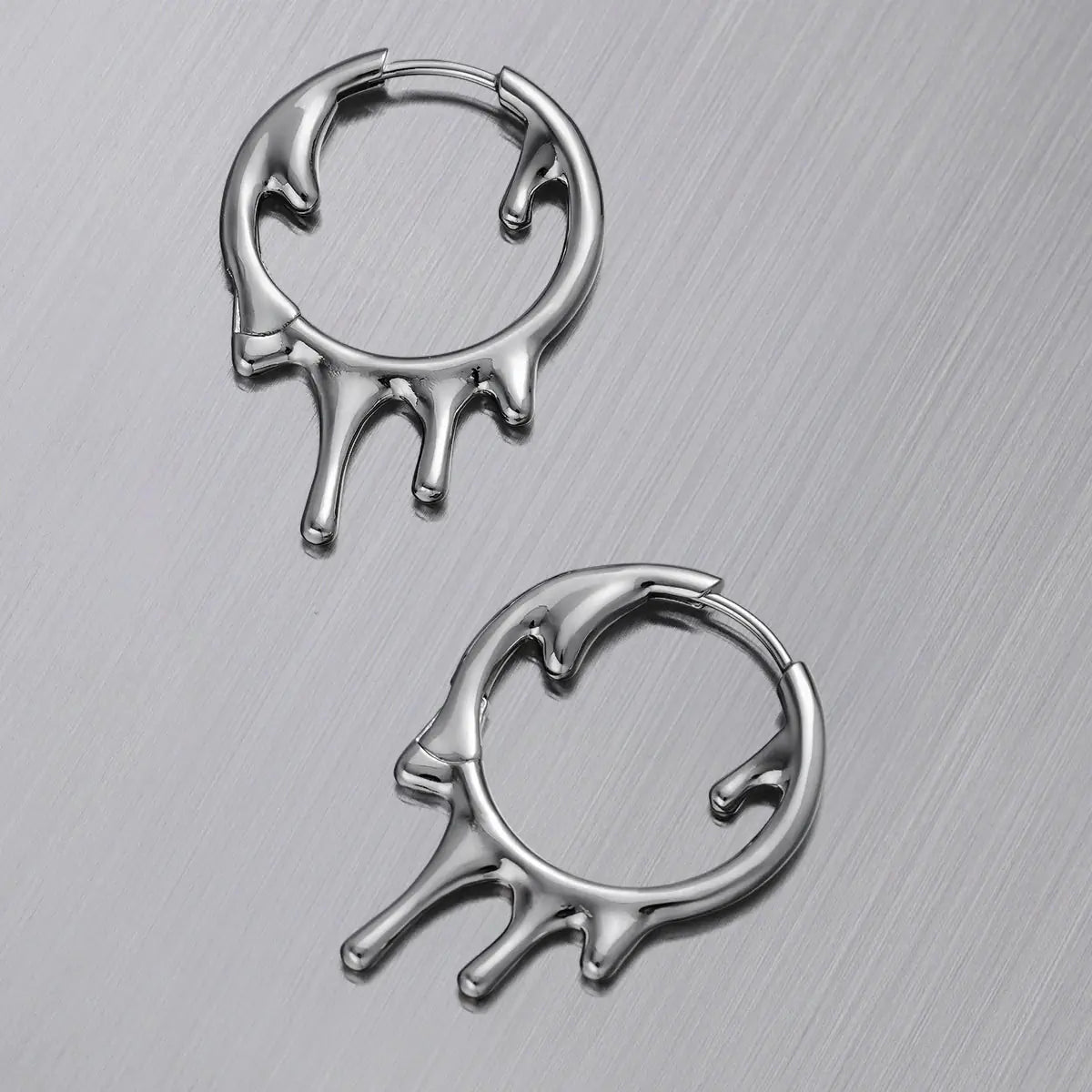 Molten Drop Earrings in 925 sterling silver, pair arranged flat on a brushed metal surface to show the molten shape from two 