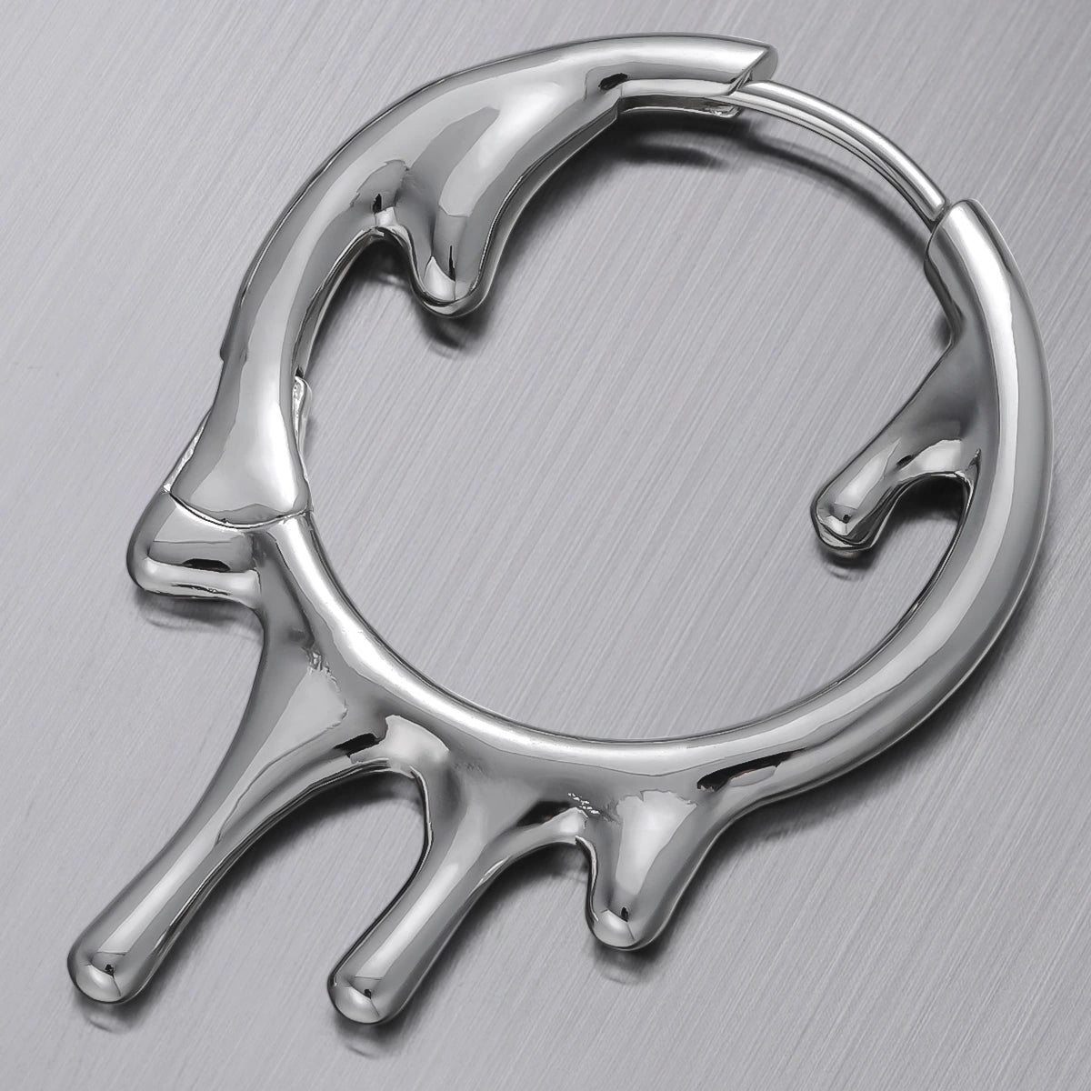 Close-up of a silver-tone hoop earring with a melted drip design resting on a metal surface