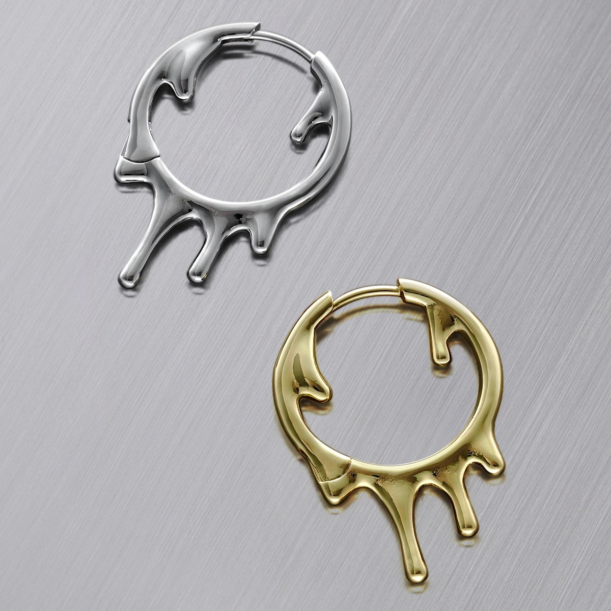 Silver-tone and gold-tone drip hoop earrings laid flat side by side on a brushed metal surface