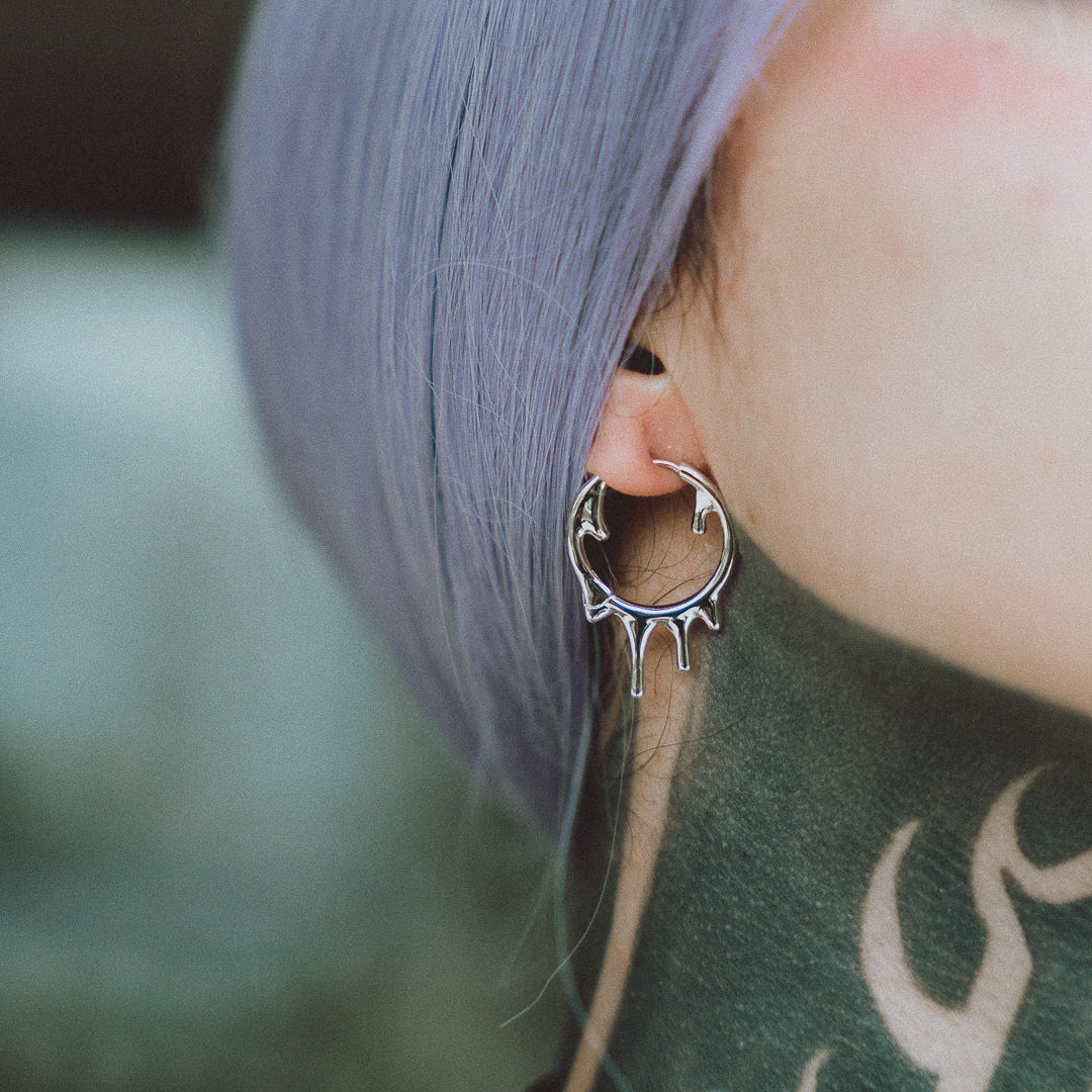 Close-up of a silver-tone drip-style hoop earring worn on a model's ear with lavender hair