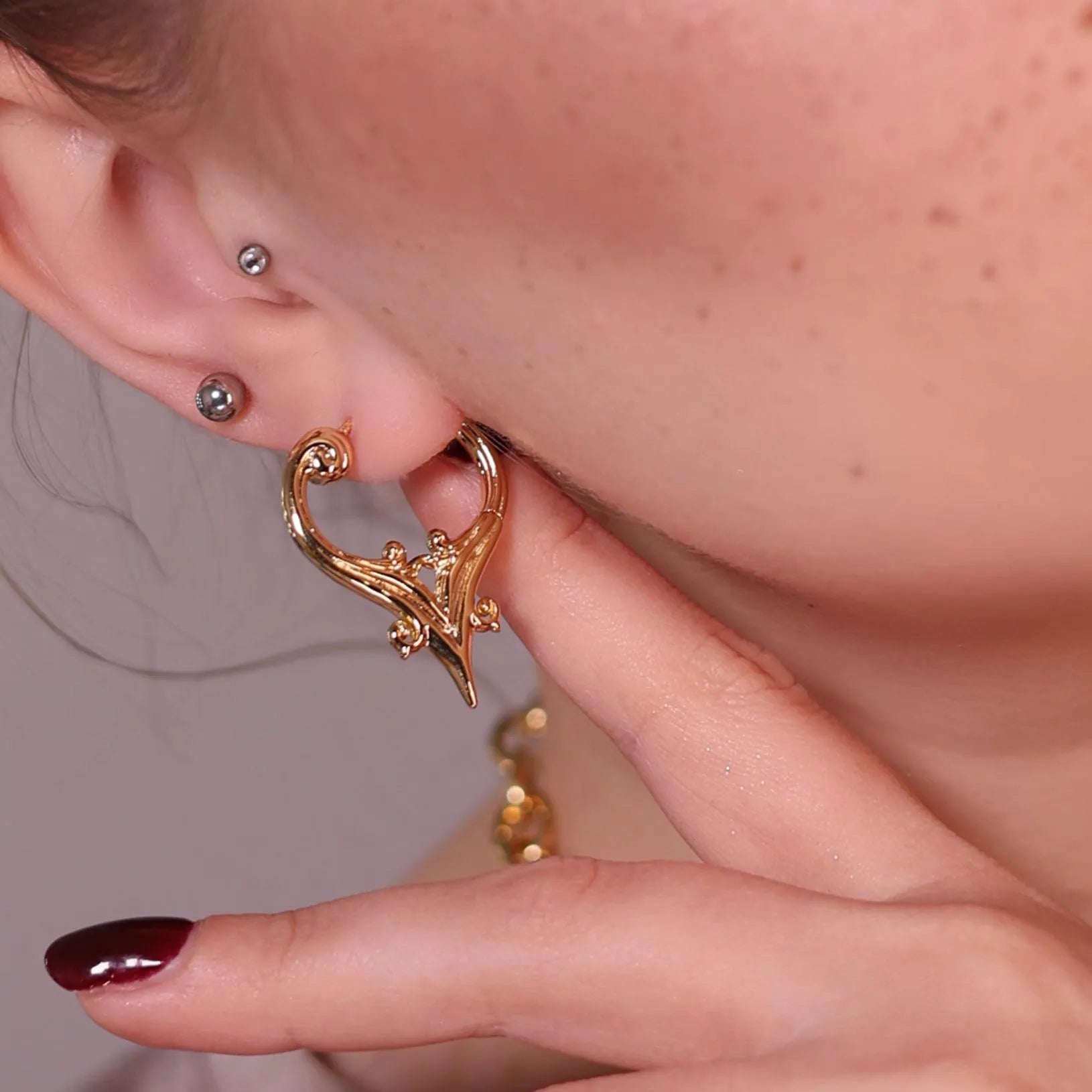 Model wearing the gold Mystic Crest Earrings with pointed shield-like silhouette, ornate scrollwork, and gothic crest styling.