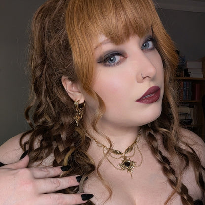 Model wearing a small gold-tone hoop earring paired with a layered necklace featuring a matching pendant