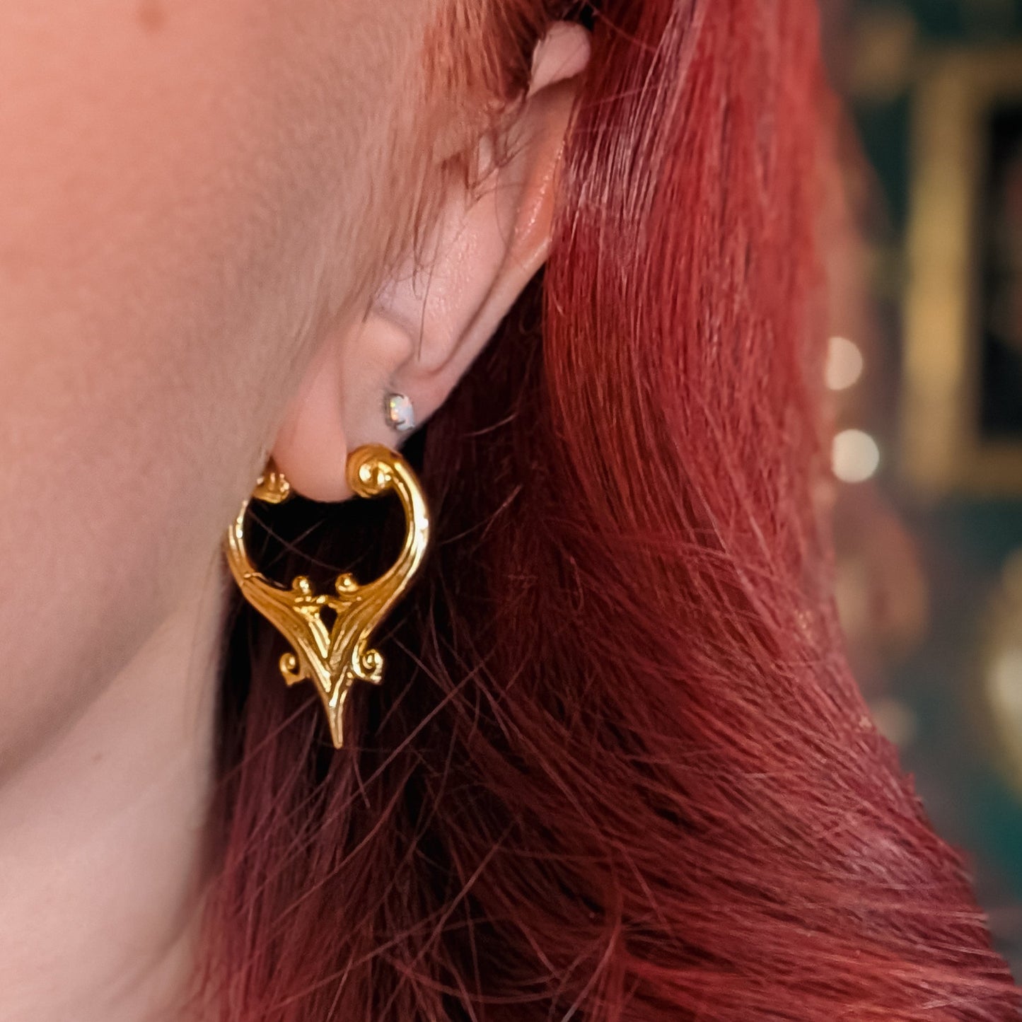 Close-up of a gold-tone crest hoop earring worn on a model's ear, layered with a small stud