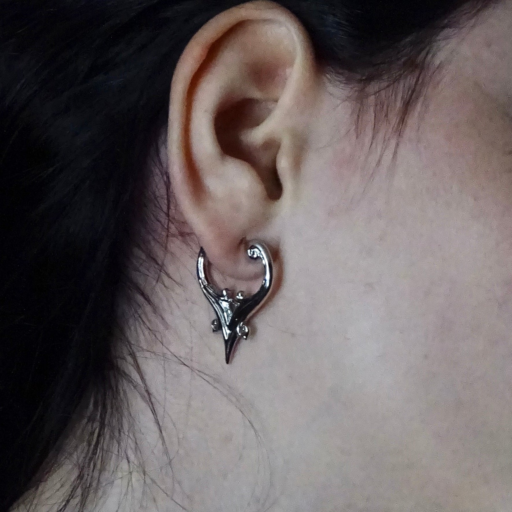 Close-up of silver Mystic Crest heart hoop earring worn on the earlobe