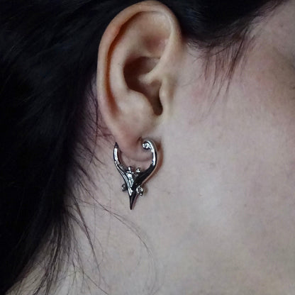 Close-up of silver Mystic Crest heart hoop earring worn on the earlobe