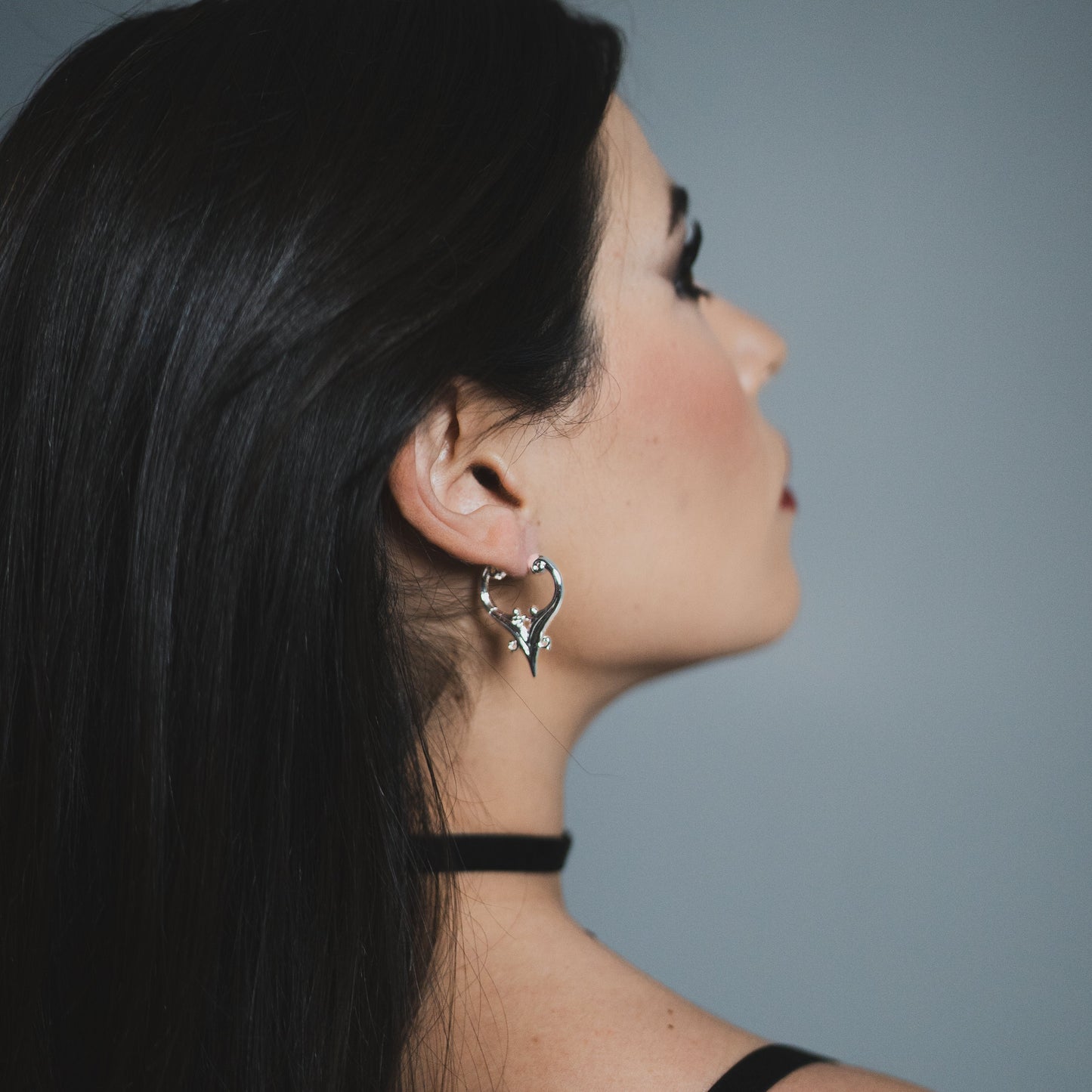Model wearing a silver Mystic Crest heart hoop earring with black choker