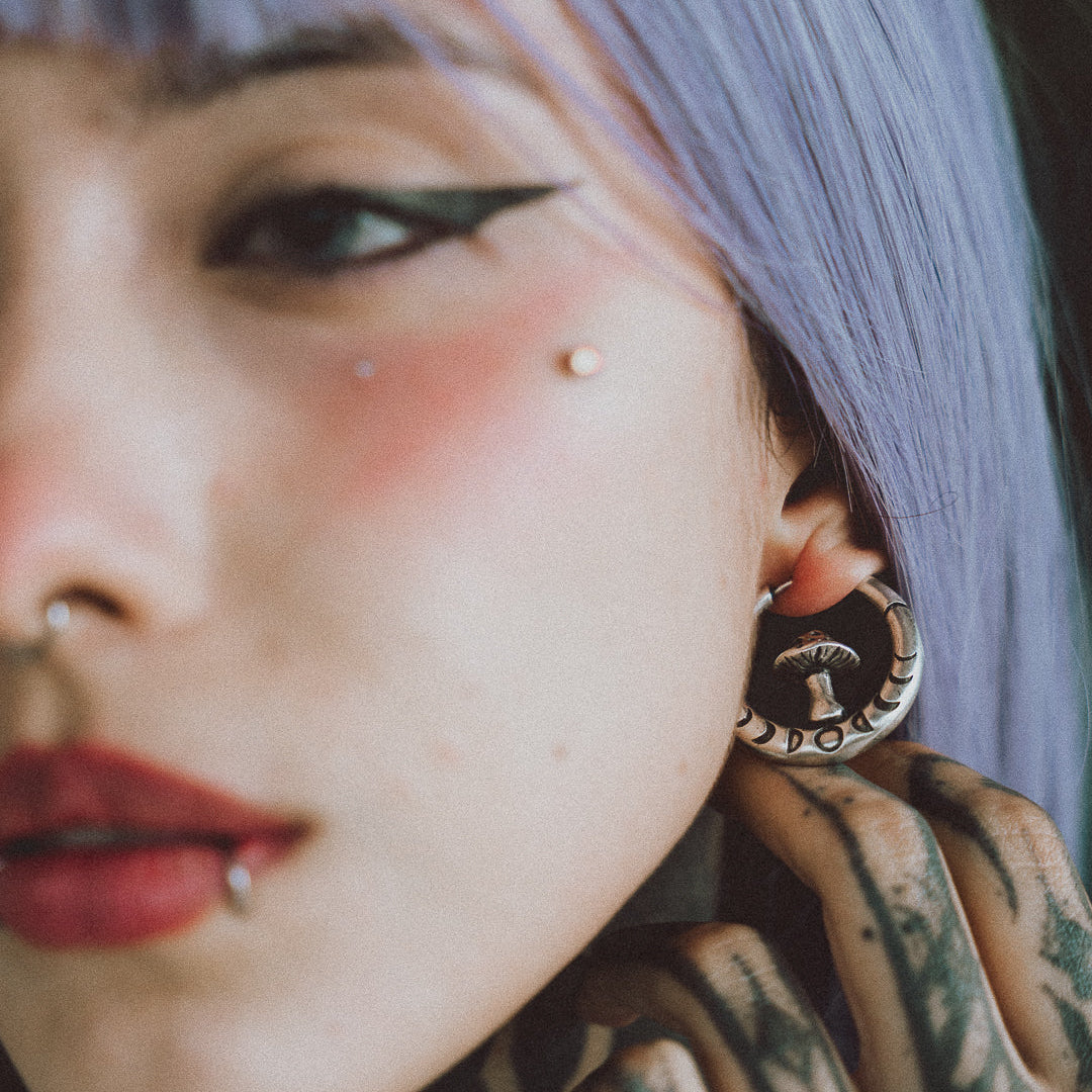 Close-up of a model wearing a silver-tone hoop earring with a small mushroom charm inside