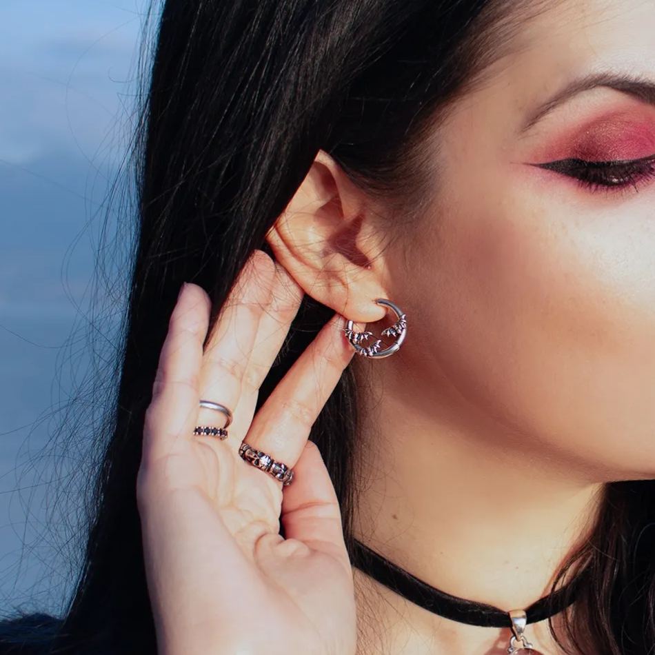 Model wears a silver-tone bat hoop earring while touching the ear with jeweled rings on the fingers