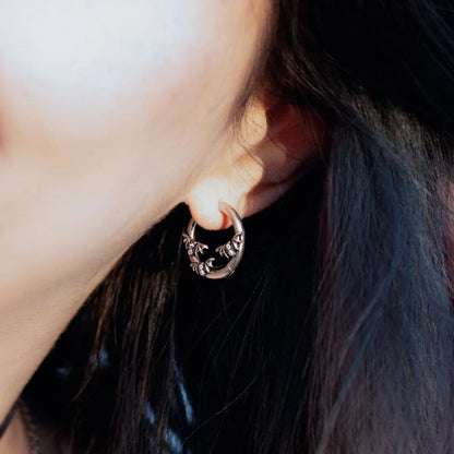 Close-up of a model wearing a silver-tone crescent hoop earring with bat detailing