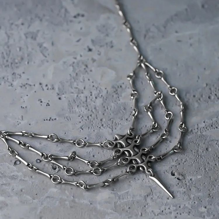 Close-up of a silver-tone spine necklace with multiple draped chains resting on a stone surface