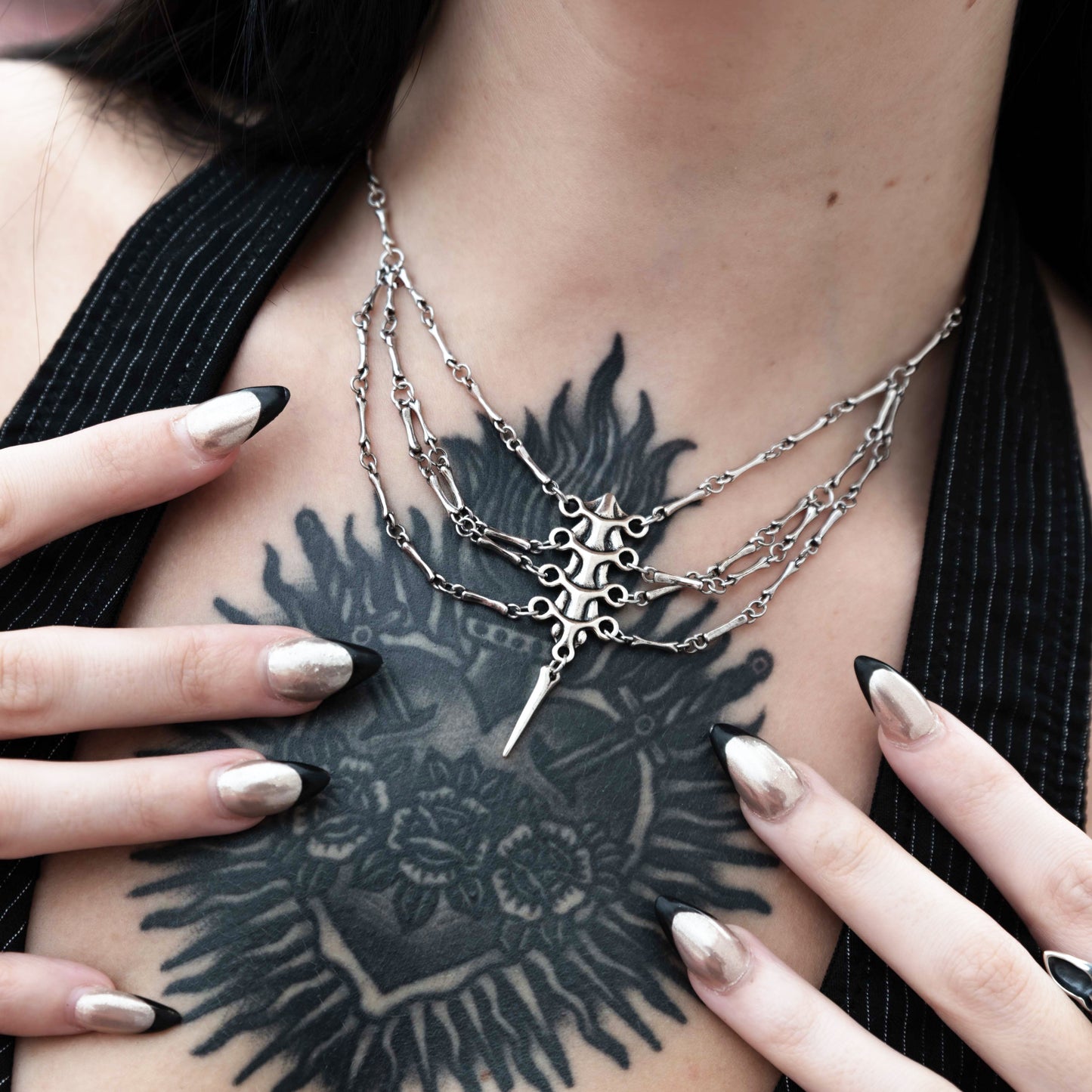 Model wears a silver-tone spine necklace with draped chains over a chest tattoo, close-up front view