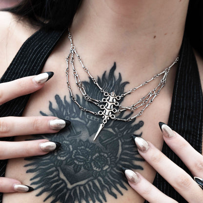 Model wears a silver-tone spine necklace with draped chains over a chest tattoo, close-up front view