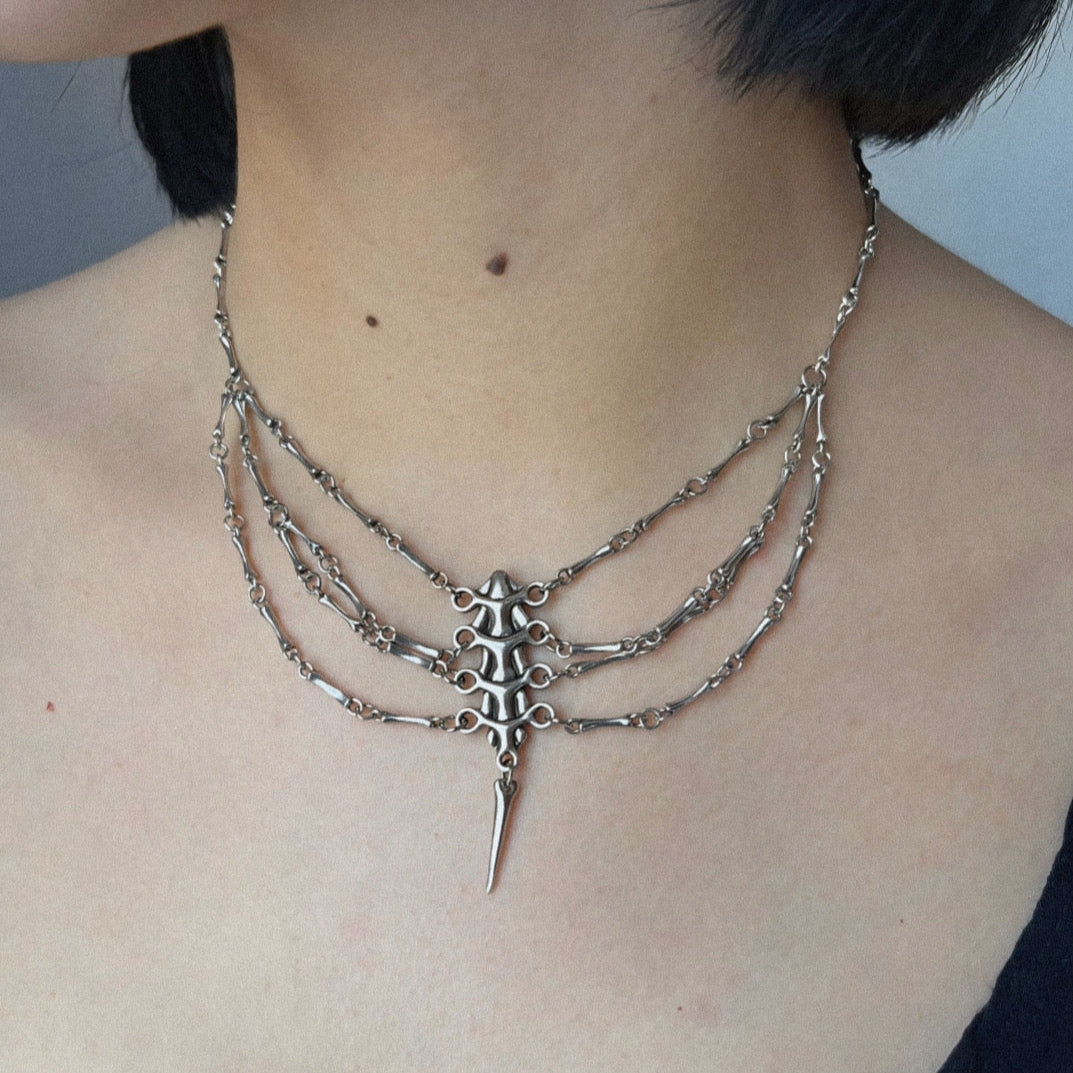 Silver-tone spine necklace with multi-strand chains worn around the neck, close-up front view