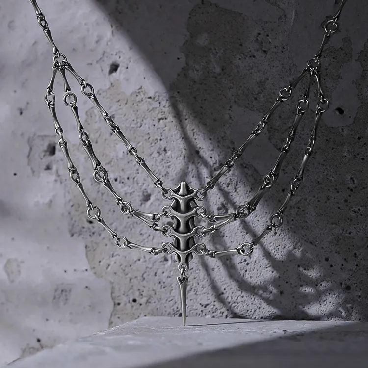 Silver-tone spine necklace with layered chains and spike pendant displayed against a textured concrete backdrop