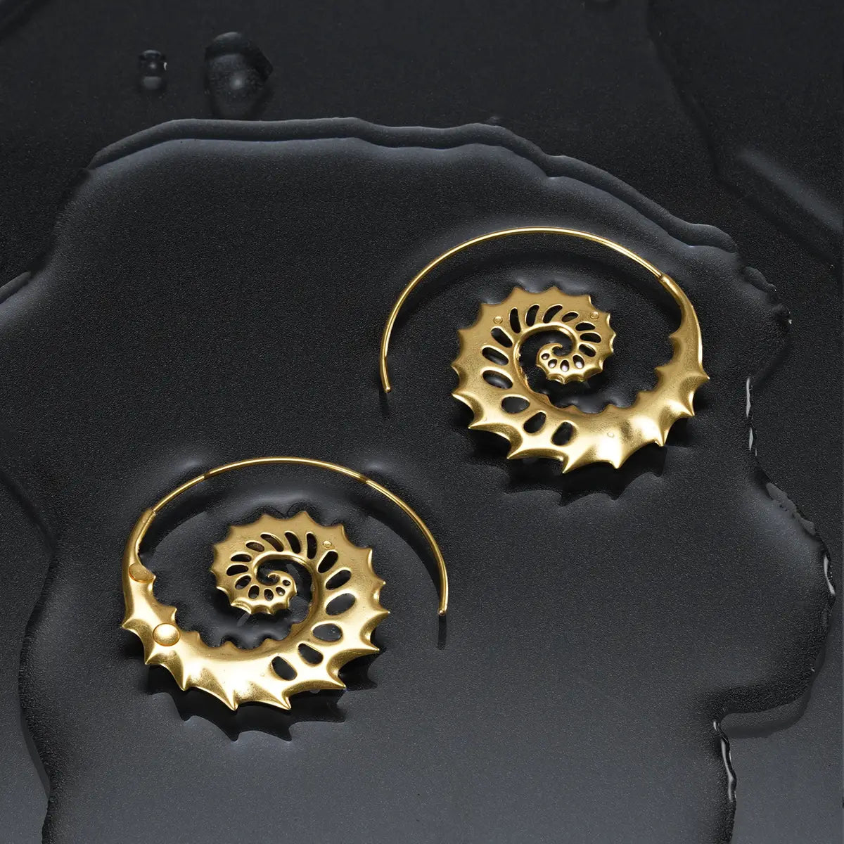 Gold Nautilus Omen Earrings displayed on a dark wet surface, featuring spiral shell shapes, cutout ridges, and coastal gothic styling.