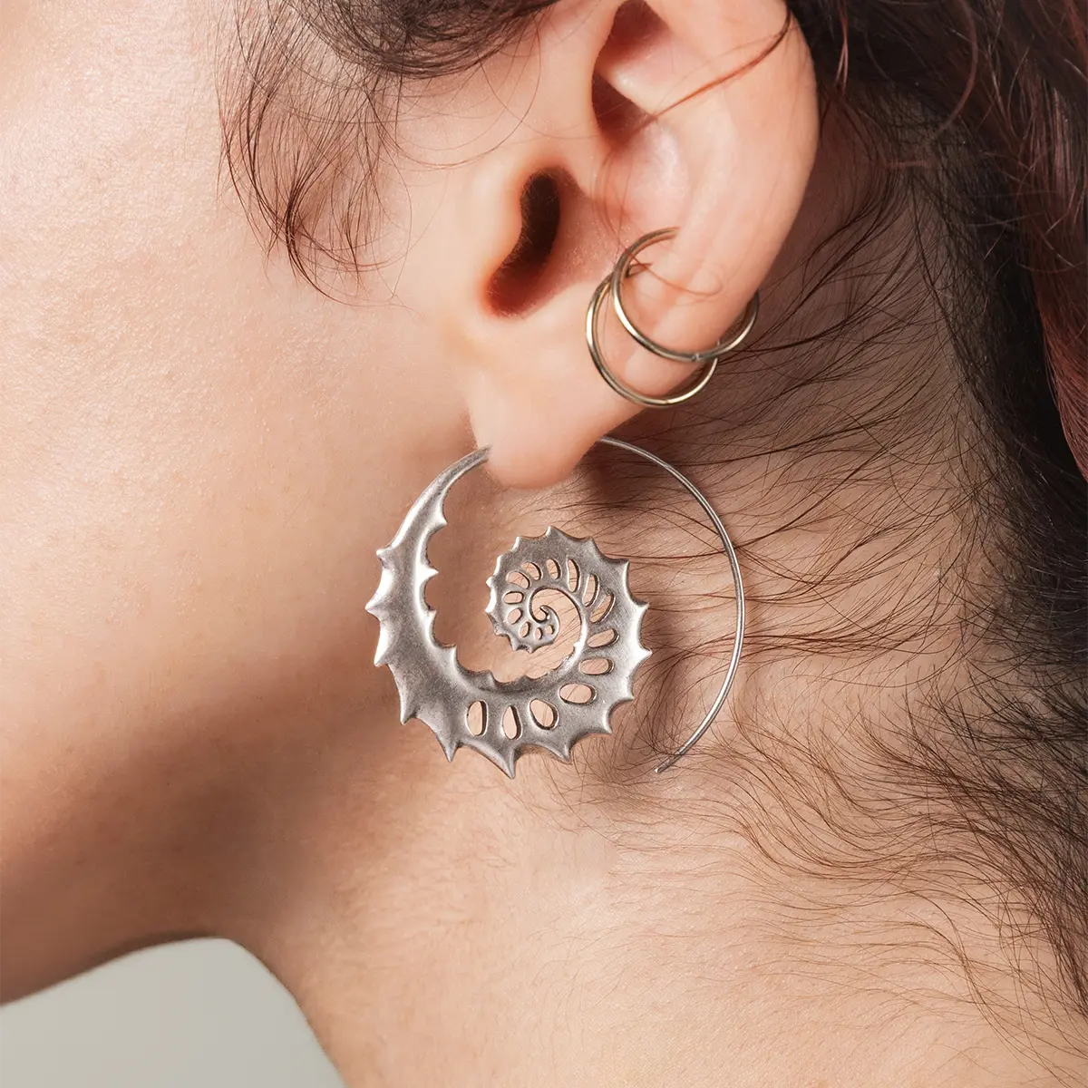 Model wearing the silver Nautilus Omen Earrings, showing the bold spiral shell profile and sharp sculptural details on the ear.