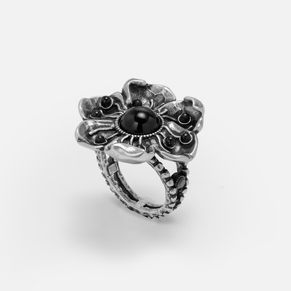 Oxidized silver-tone flower ring with a round black stone center, angled view on white background