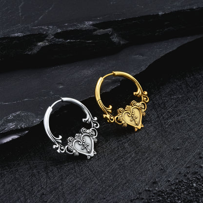Silver-tone and gold-tone hoop earrings with heart and cross motif displayed on a dark stone surface