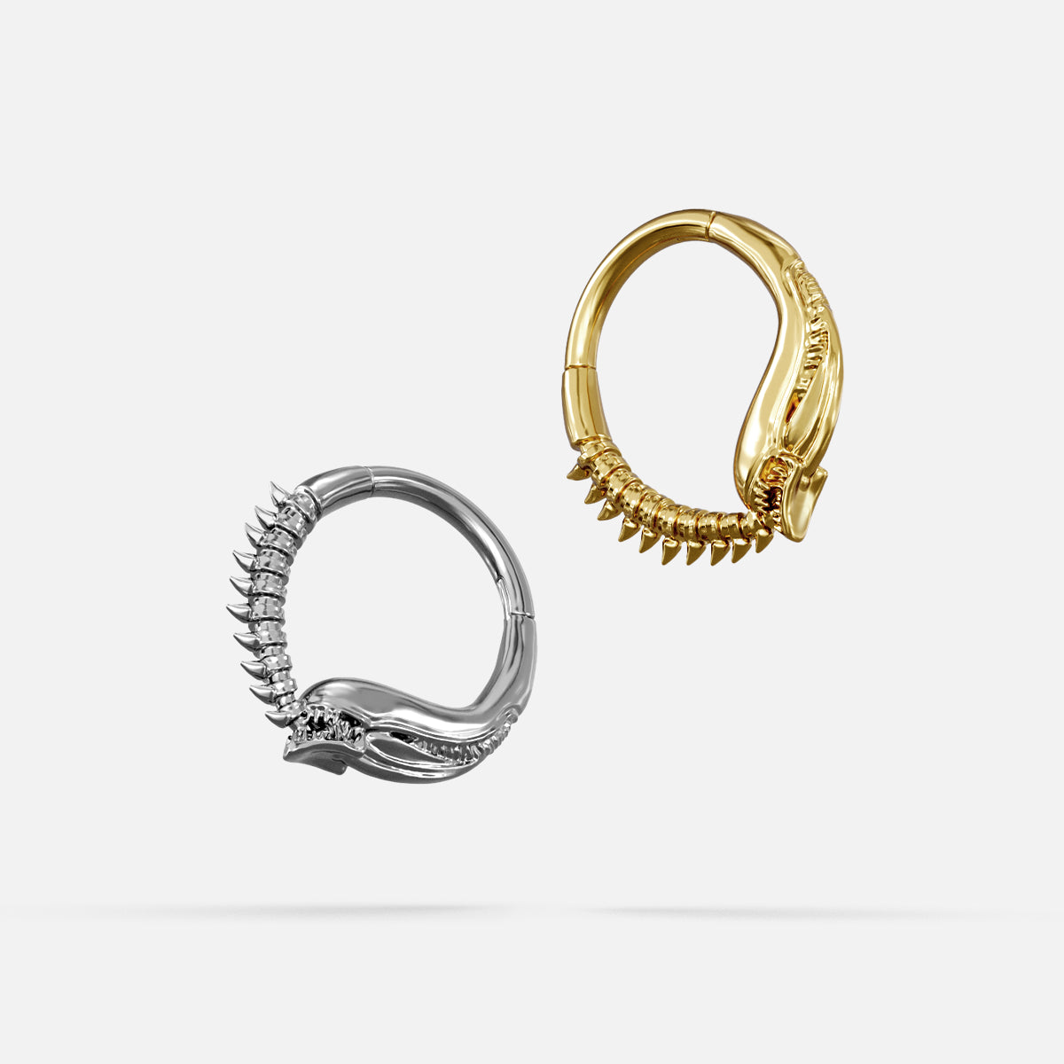 Silver- and gold-tone Ouroboros Clickers displayed together from angled views on a light gray background.