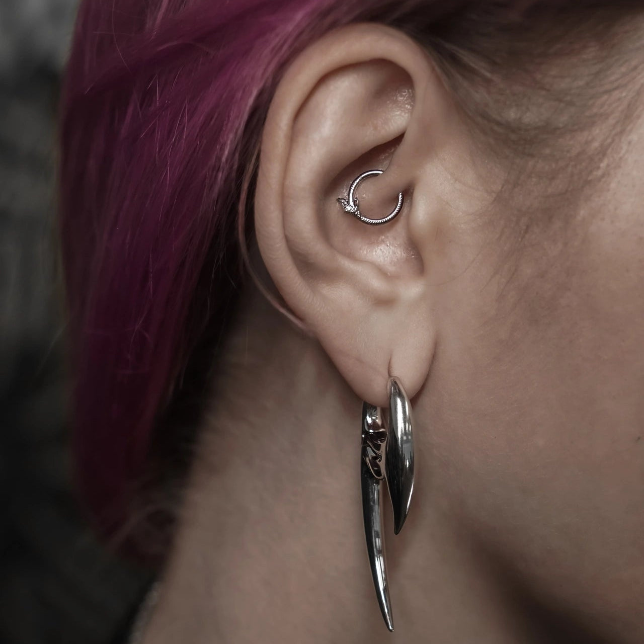 ouroboros coil clicker worn in the inner ear in a close-up view, featuring a silver snake-inspired circular clicker