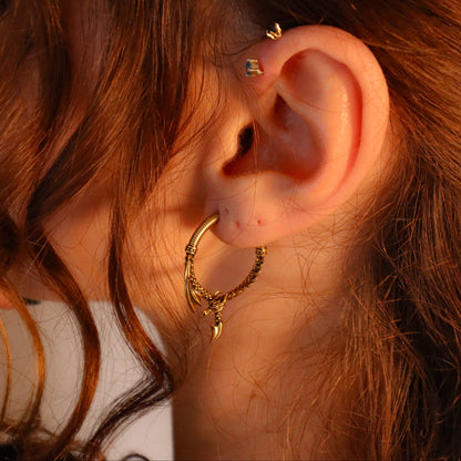 Gold-tone dragon hoop earring worn in a model's ear with a small stud in the upper lobe