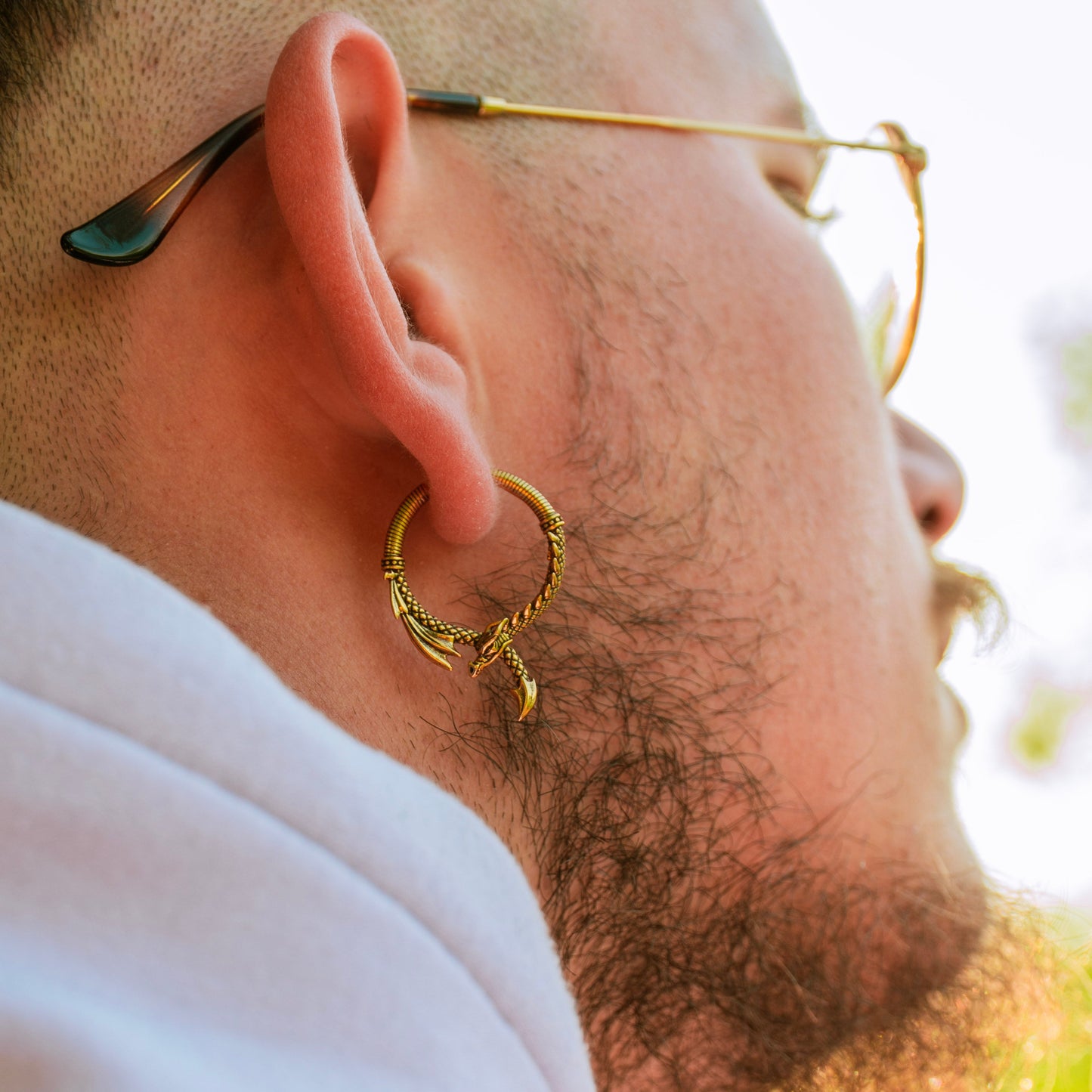 Gold-tone dragon hoop earring worn by a model with glasses, close-up side view