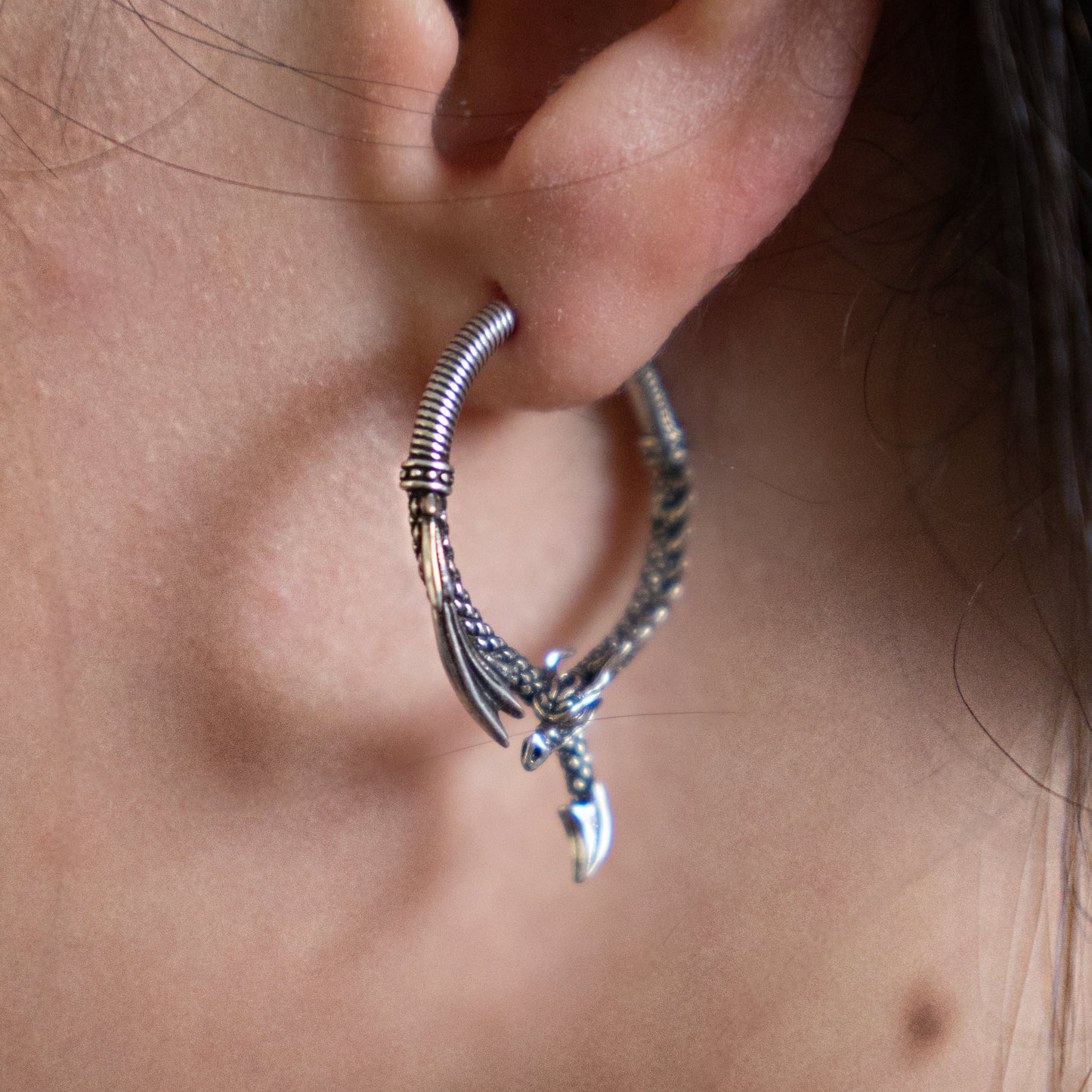 Silver-tone dragon hoop earring worn in a close-up view of a model's ear