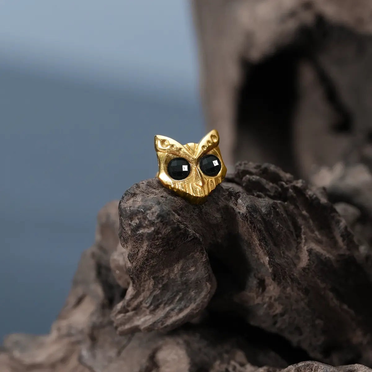 Gold Owl Skull Ear Studs displayed on driftwood with black obsidian eyes and gothic owl design