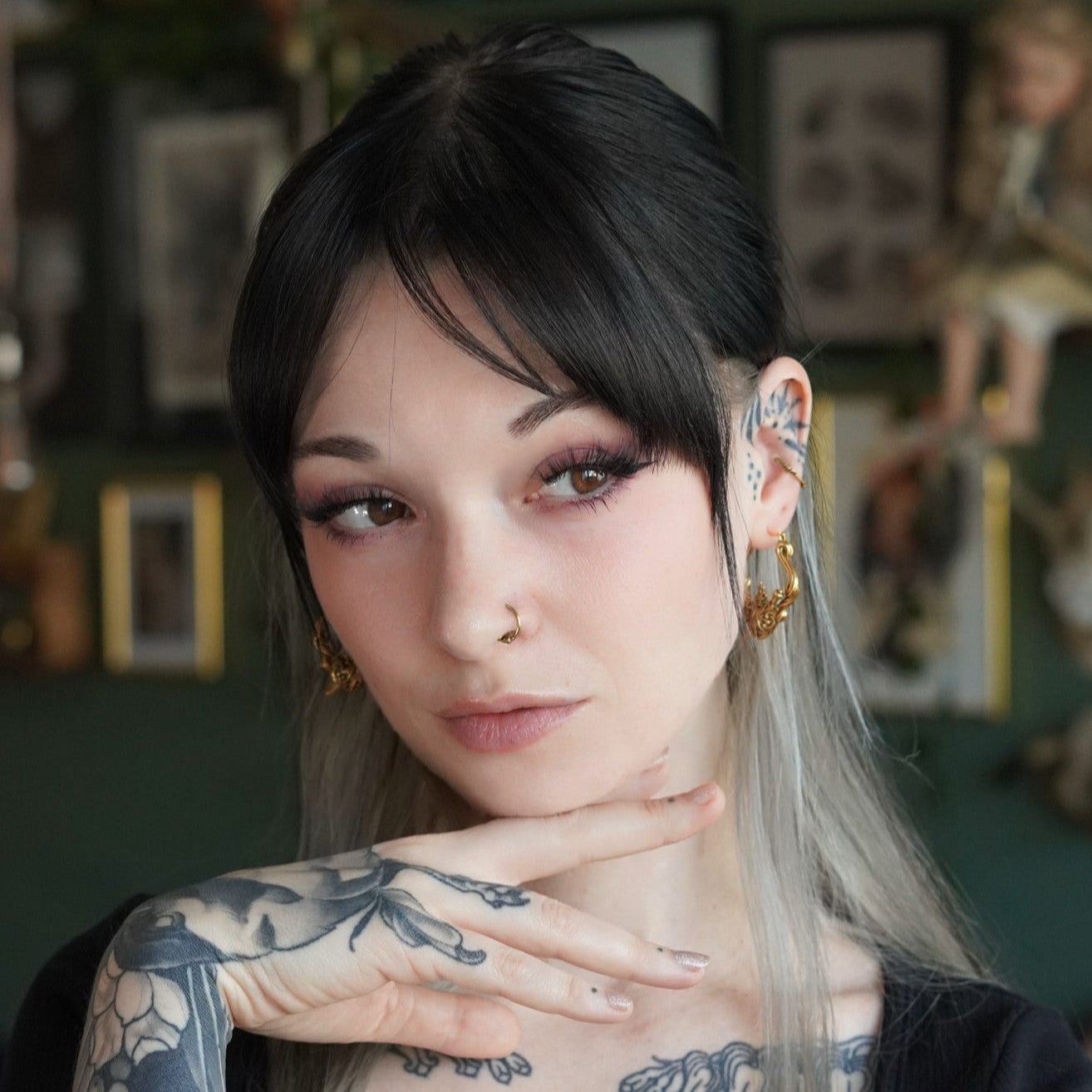 Person with tattooed neck and gray-black hair wearing a small gold-tone heart hoop earring