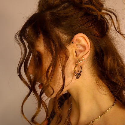 Side profile of a person with wavy hair wearing a gold-tone heart-shaped hoop earring among multiple ear piercings