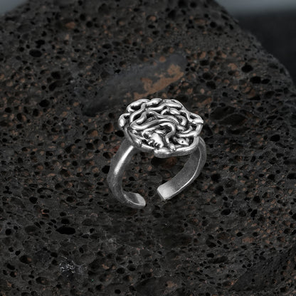 petrified gaze rings in silver shown in an angled product view on black volcanic rock, featuring a medusa-inspired face surrounded by sculpted snake details