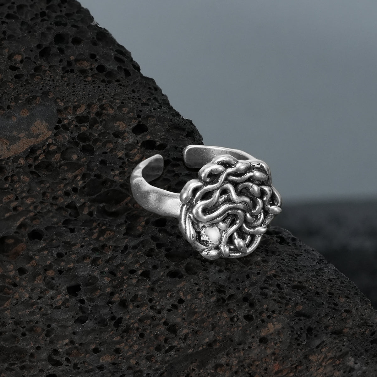 petrified gaze rings in silver shown in a product view on black volcanic rock, featuring a medusa-inspired face surrounded by sculpted snake details