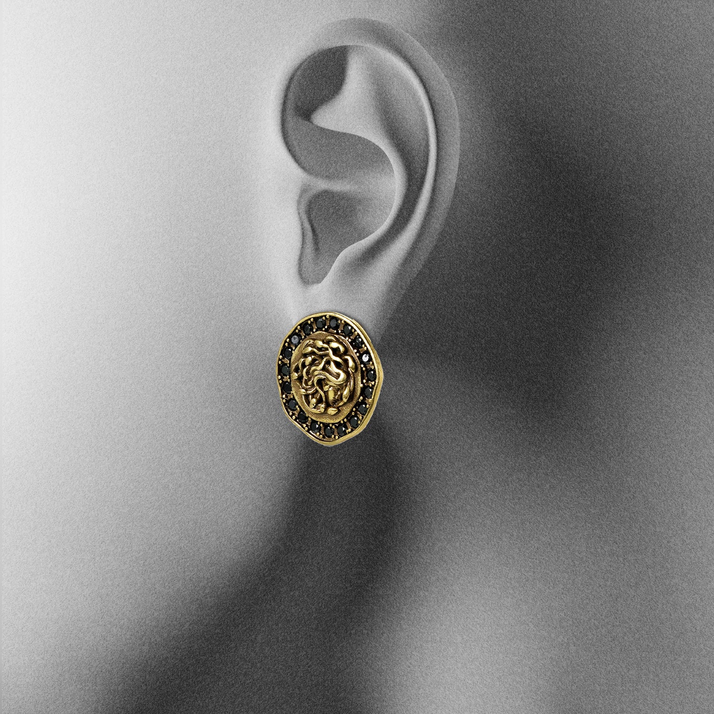 gold petrified nocturne ear studs shown on an ear display, featuring a medusa-inspired face framed with black cubic zirconia