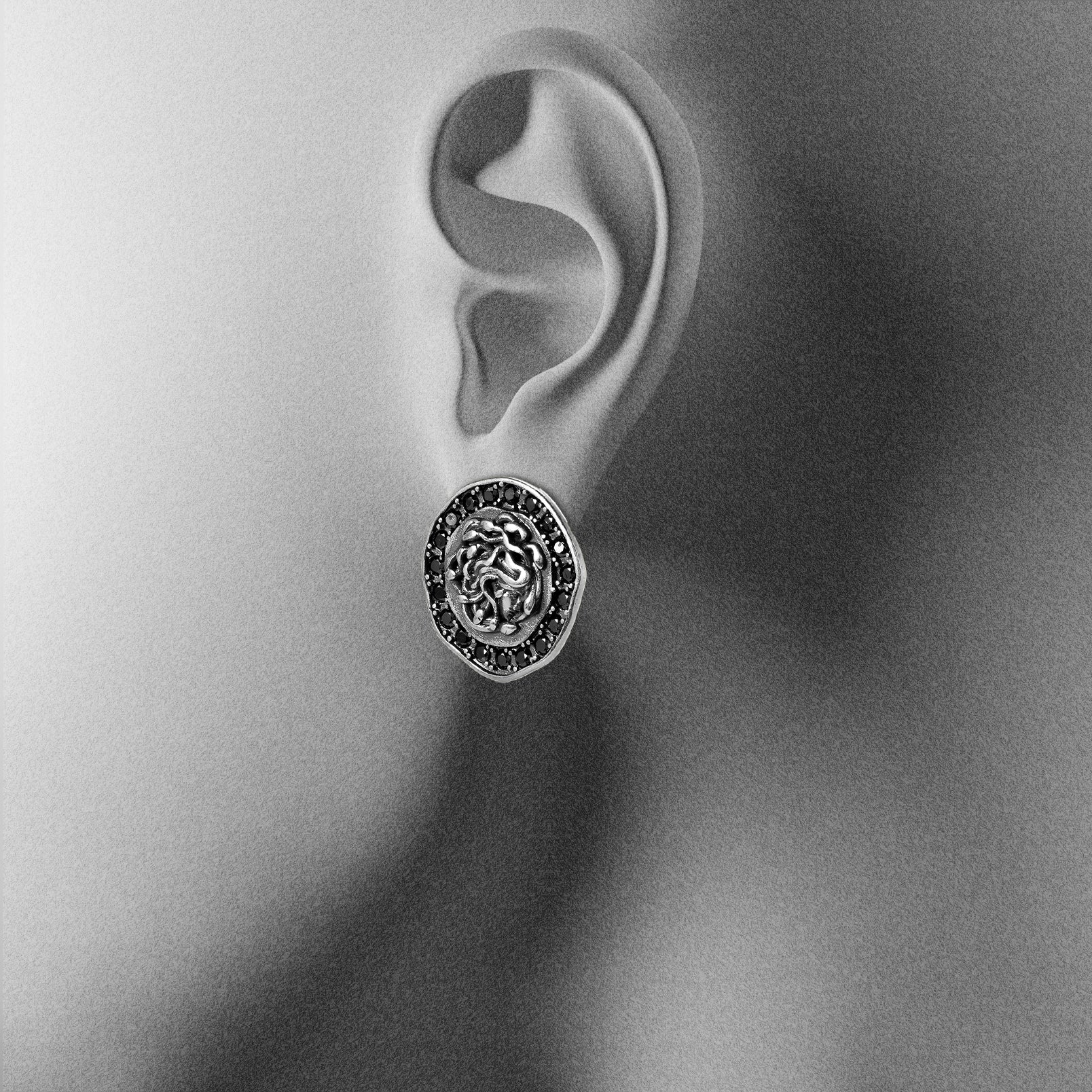 silver petrified nocturne ear studs shown on an ear display, featuring a medusa-inspired face framed with black cubic zirconia