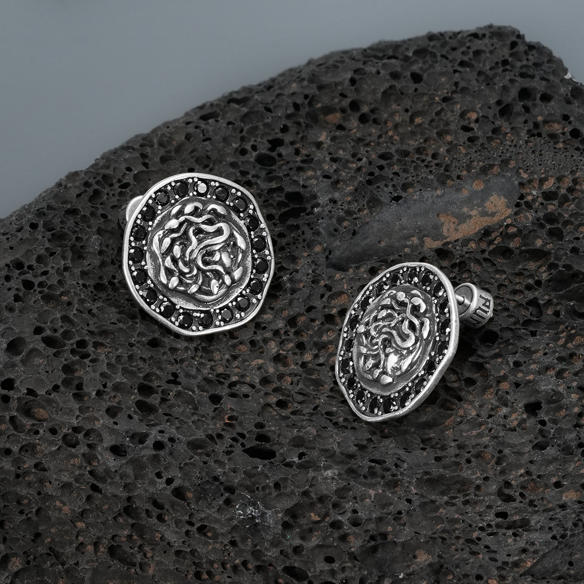 petrified nocturne ear studs in silver shown in a product view on black volcanic rock, featuring medusa-inspired ear studs framed with black cubic zirconia