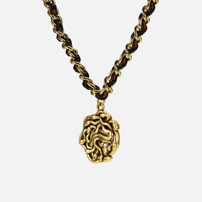 petrified power necklace in gold shown in an angled close-up view, featuring a medusa-inspired pendant on a braided chain