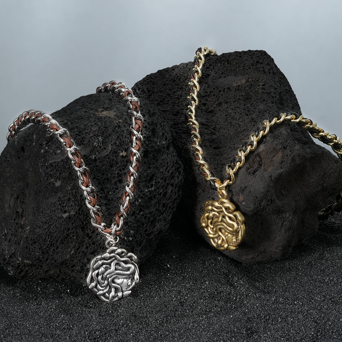 petrified power necklace shown in silver and gold in a product view on black volcanic rock, featuring medusa-inspired pendants on braided chains
