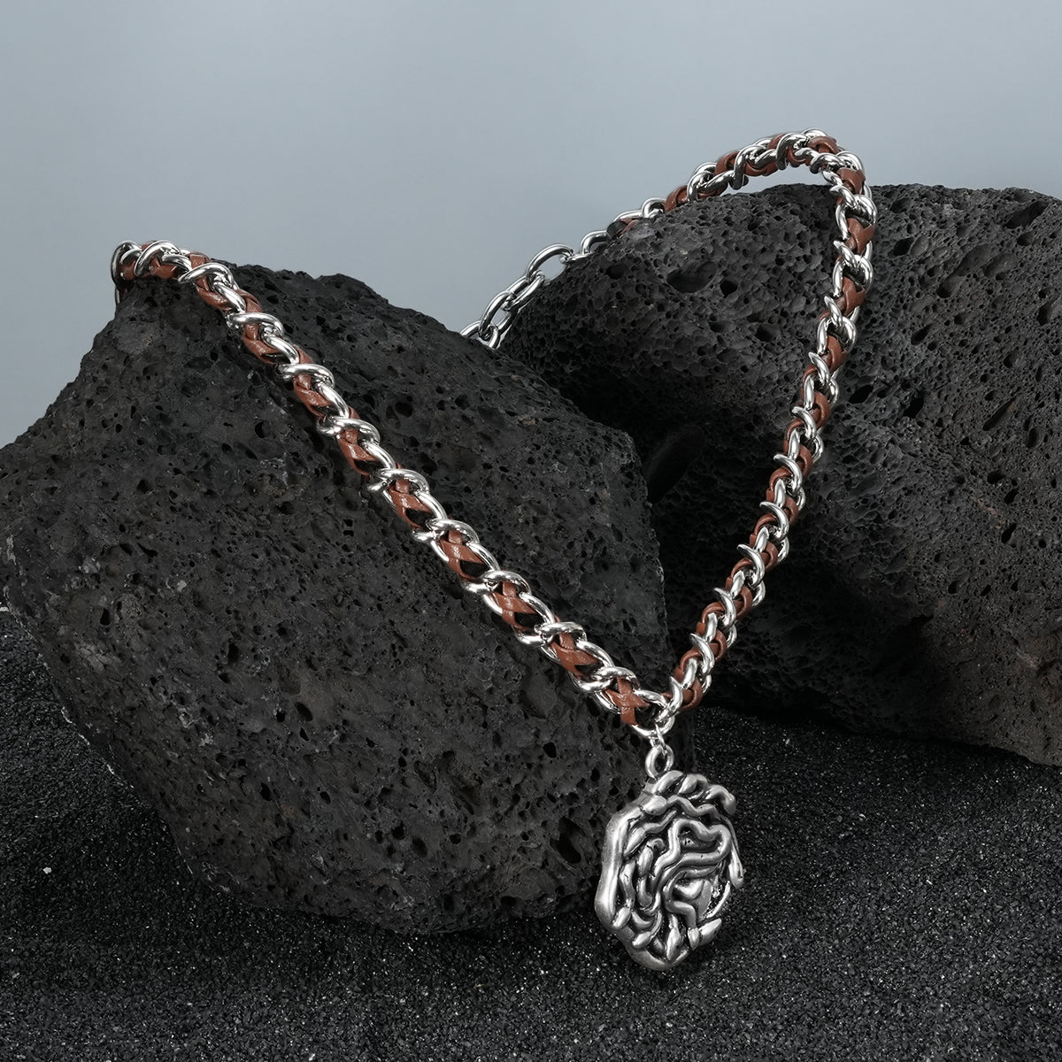 petrified power necklace in silver shown in a product view on black volcanic rock, featuring a medusa-inspired pendant on a braided chain