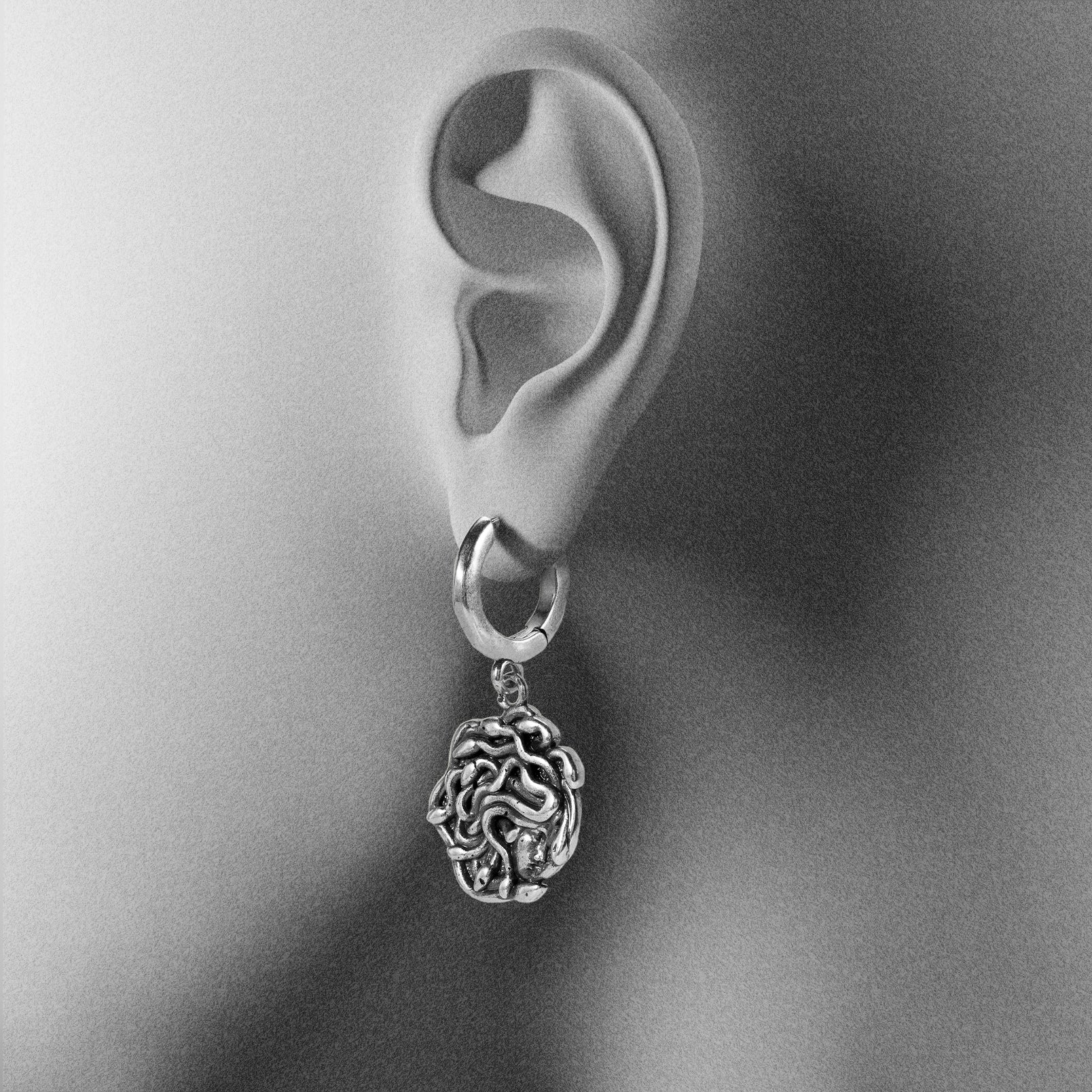 silver petrifying gaze dangle earrings shown on an ear display, featuring a medusa-inspired charm suspended from a hoop