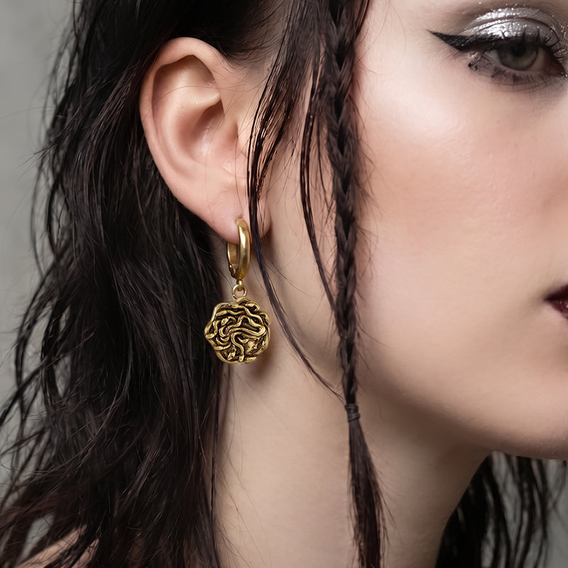 model wearing petrifying gaze dangle earrings in gold, featuring a medusa-inspired charm suspended from a hoop