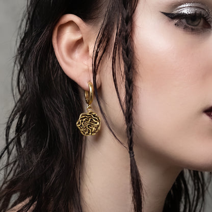 model wearing petrifying gaze dangle earrings in gold, featuring a medusa-inspired charm suspended from a hoop