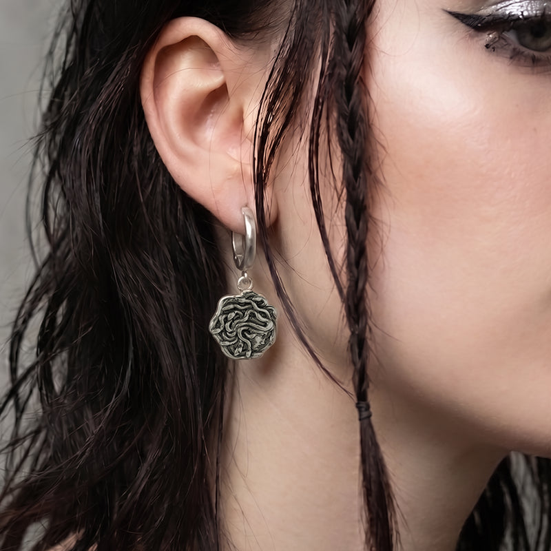 model wearing petrifying gaze dangle earrings in silver, featuring a medusa-inspired charm suspended from a hoop